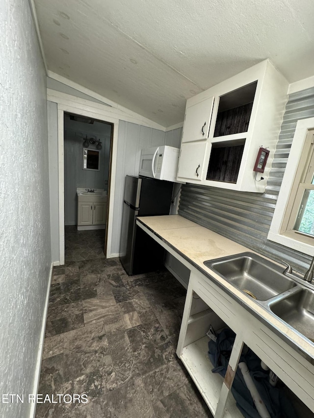 kitchen featuring stainless steel refrigerator, sink, a textured ceiling, vaulted ceiling, and white cabinets