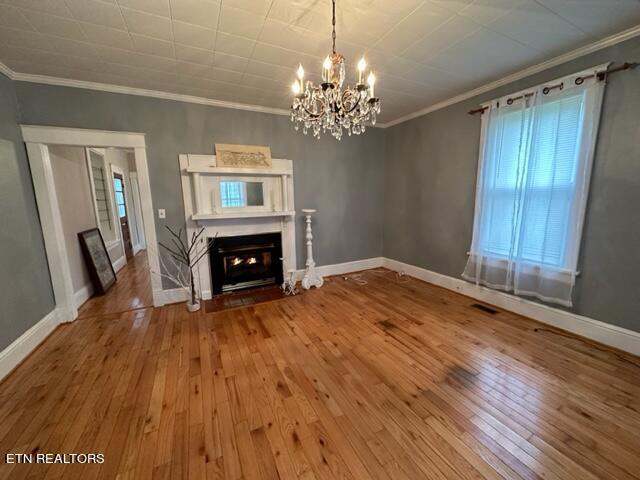 unfurnished living room with hardwood / wood-style floors, ornamental molding, and an inviting chandelier