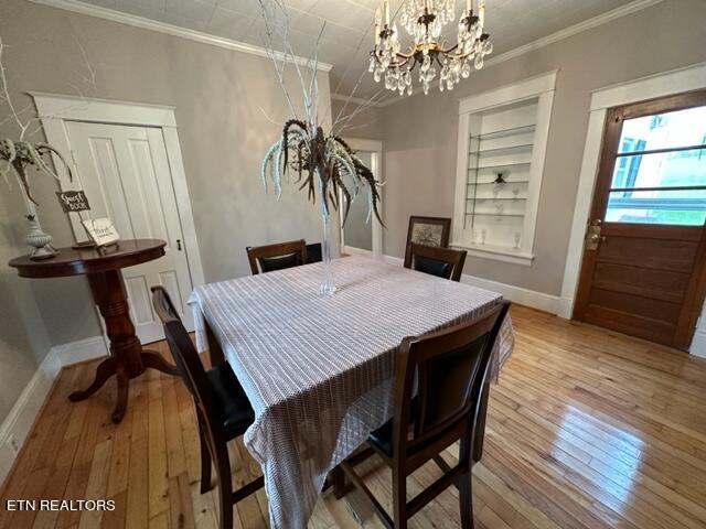 dining room with crown molding, built in features, light hardwood / wood-style floors, and a notable chandelier