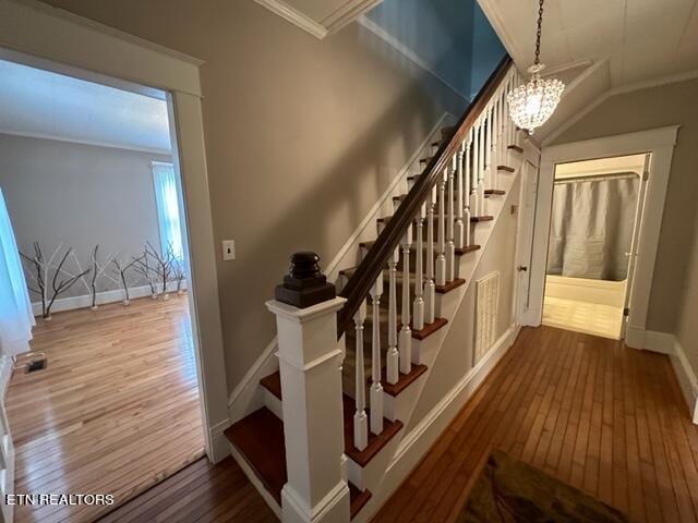 staircase with hardwood / wood-style floors, a chandelier, crown molding, and vaulted ceiling