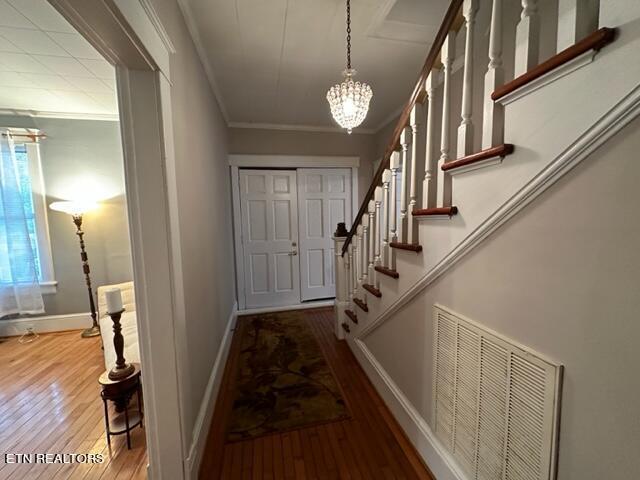 entryway with a chandelier, wood-type flooring, and crown molding