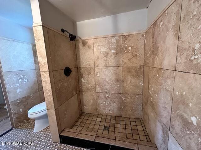 bathroom with a tile shower, toilet, tile walls, and tile patterned floors