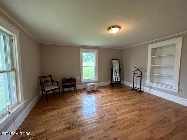 unfurnished room featuring a wall mounted air conditioner, built in shelves, hardwood / wood-style flooring, and ornamental molding