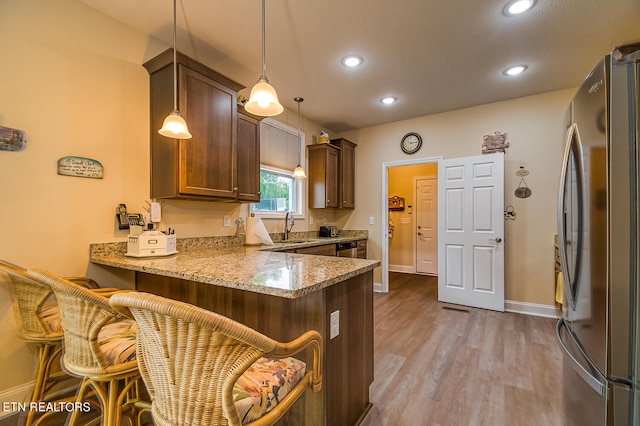 kitchen with pendant lighting, a kitchen breakfast bar, light stone counters, kitchen peninsula, and stainless steel appliances