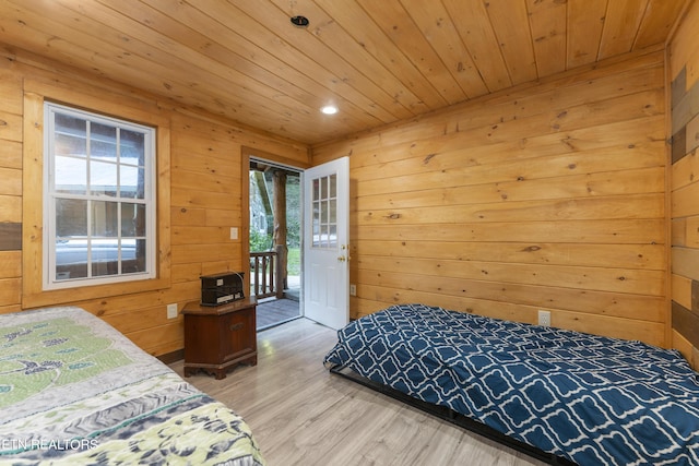 bedroom featuring access to outside, light hardwood / wood-style flooring, multiple windows, and wooden walls