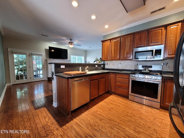 kitchen featuring ceiling fan, backsplash, kitchen peninsula, appliances with stainless steel finishes, and light wood-type flooring