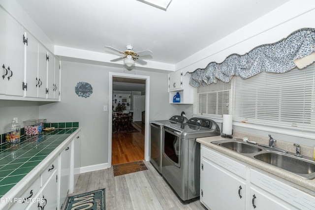 clothes washing area featuring ceiling fan, sink, cabinets, washer and dryer, and light wood-type flooring