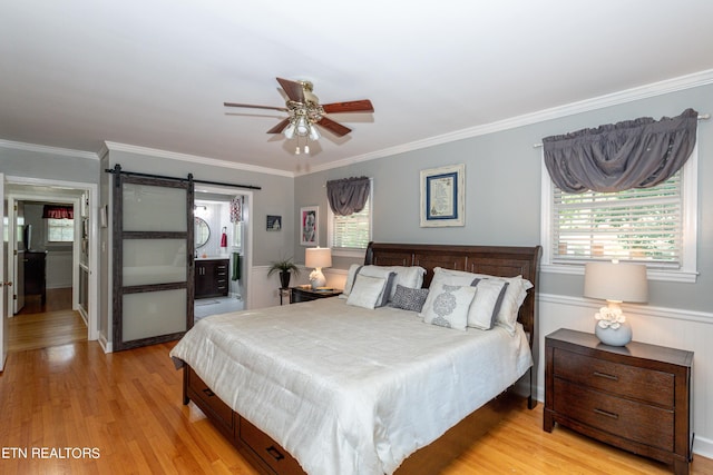 bedroom featuring crown molding, light hardwood / wood-style flooring, ensuite bath, ceiling fan, and a barn door