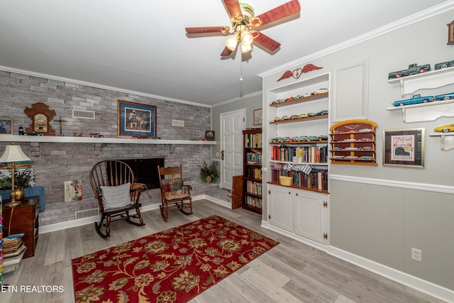 living area with a brick fireplace, ceiling fan, ornamental molding, light hardwood / wood-style floors, and brick wall