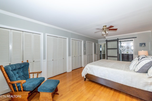 bedroom with light wood-type flooring, ceiling fan, crown molding, a barn door, and multiple closets