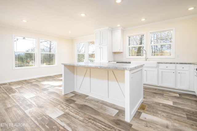 kitchen with white cabinets, a center island, sink, light stone counters, and crown molding