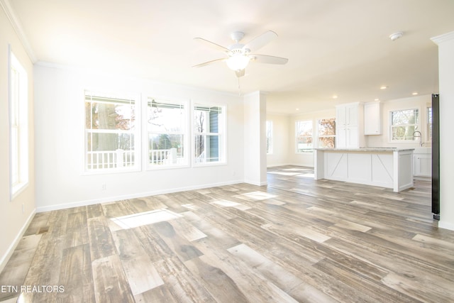 unfurnished living room featuring ceiling fan, plenty of natural light, light hardwood / wood-style flooring, and crown molding