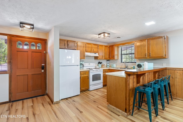 kitchen with white appliances, sink, light hardwood / wood-style flooring, a kitchen bar, and kitchen peninsula