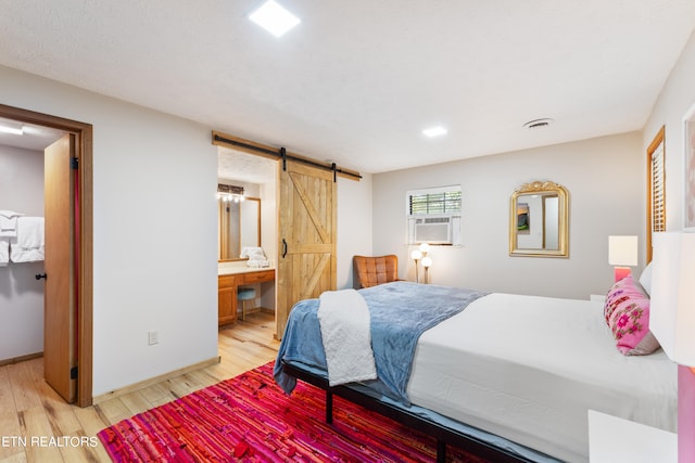 bedroom with a barn door, ensuite bathroom, cooling unit, and light hardwood / wood-style floors