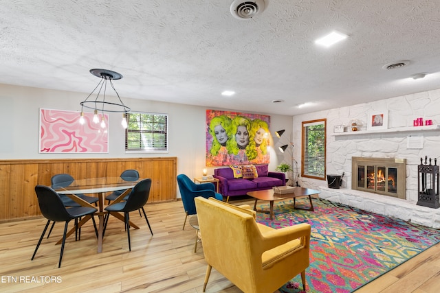 living room featuring a stone fireplace, light wood-type flooring, a textured ceiling, and a wealth of natural light