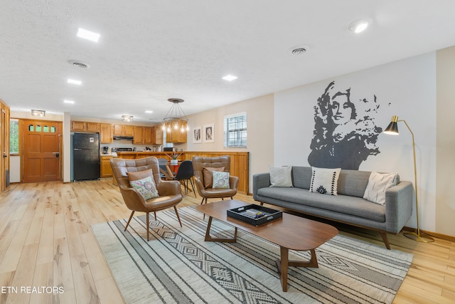 living room with a chandelier, a textured ceiling, and light wood-type flooring