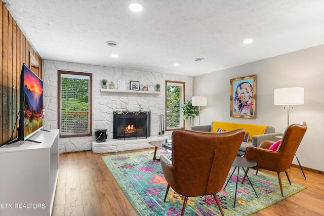 living room with hardwood / wood-style floors, a textured ceiling, a stone fireplace, and plenty of natural light