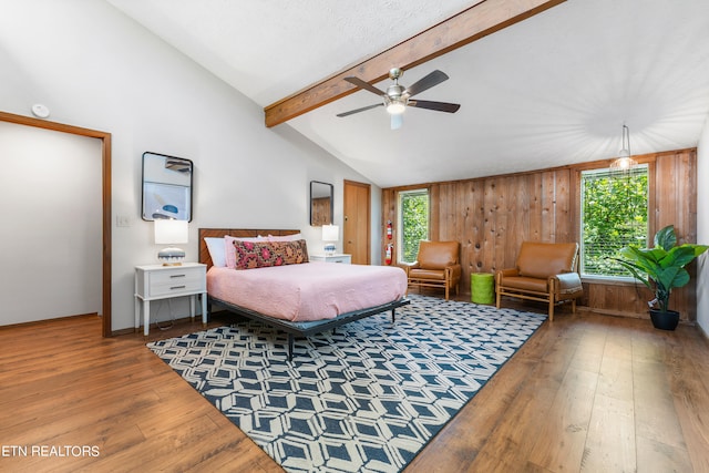 bedroom with hardwood / wood-style floors, ceiling fan, wood walls, and lofted ceiling with beams