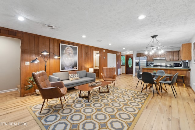 living room with wood walls, sink, a textured ceiling, and light hardwood / wood-style flooring