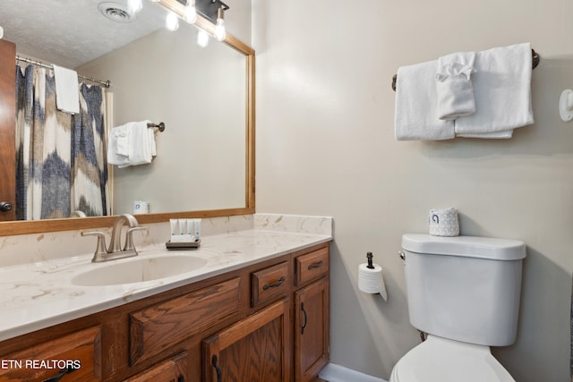 bathroom with a textured ceiling, vanity, and toilet