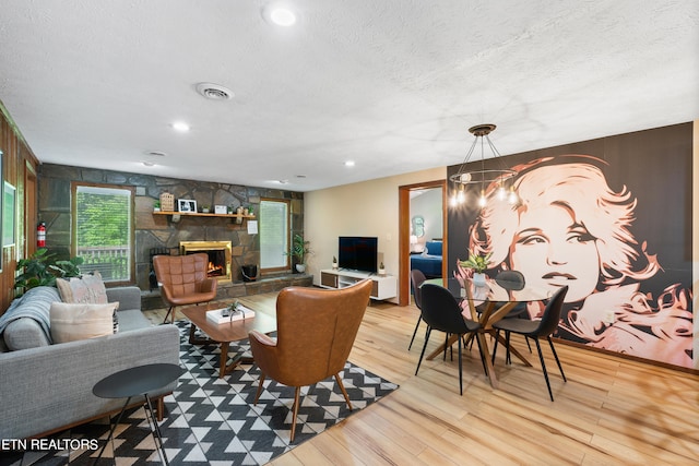 living room with a stone fireplace, an inviting chandelier, a textured ceiling, and light wood-type flooring