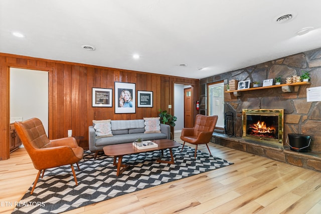 living room with light hardwood / wood-style floors, a stone fireplace, and wood walls