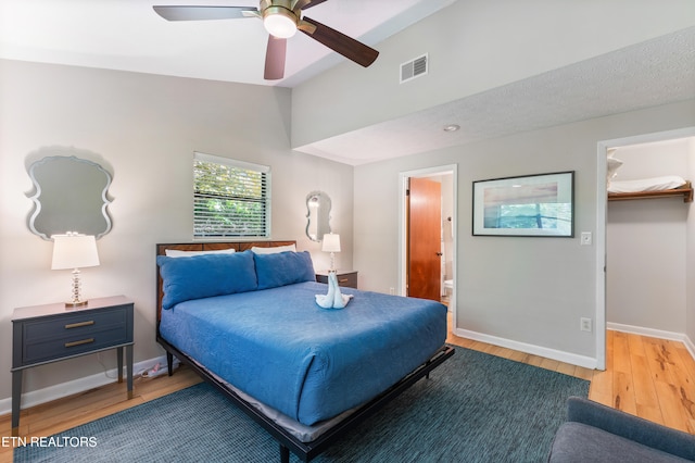 bedroom featuring hardwood / wood-style floors, lofted ceiling, ensuite bathroom, ceiling fan, and a spacious closet