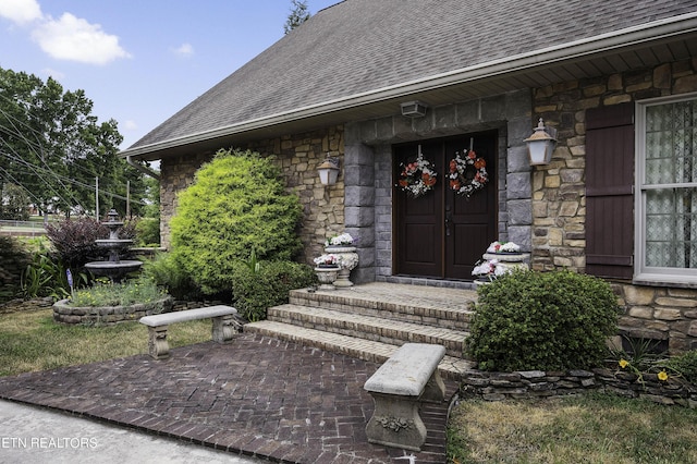 entrance to property with stone siding and a shingled roof