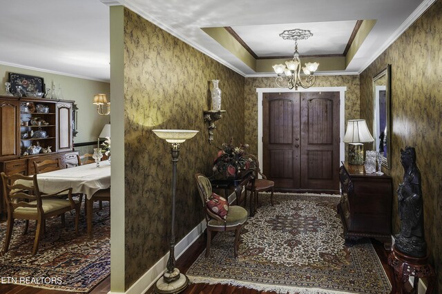 foyer entrance with a tray ceiling, crown molding, a chandelier, and wood-type flooring