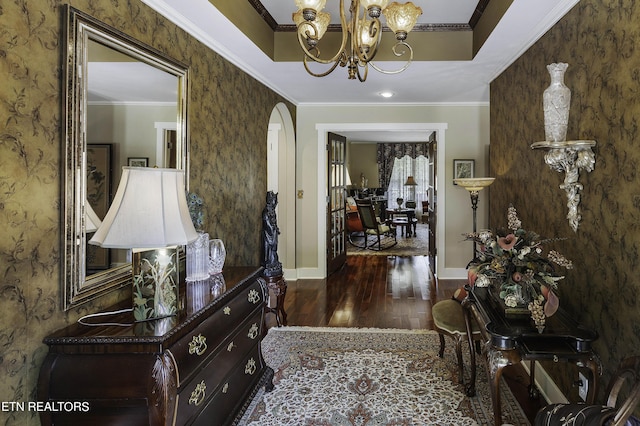 entrance foyer featuring wood finished floors, baseboards, arched walkways, ornamental molding, and a chandelier