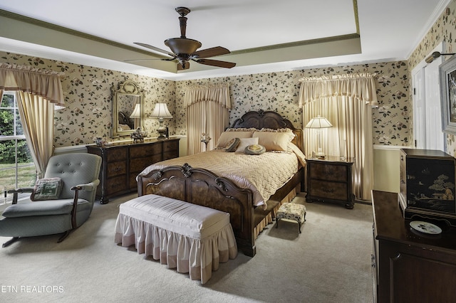 bedroom with wallpapered walls, a tray ceiling, ornamental molding, ceiling fan, and light carpet