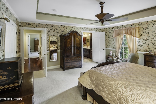 bedroom featuring a tray ceiling, connected bathroom, crown molding, wallpapered walls, and light colored carpet