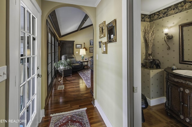 hallway with wood finished floors, arched walkways, wallpapered walls, baseboards, and vaulted ceiling with beams