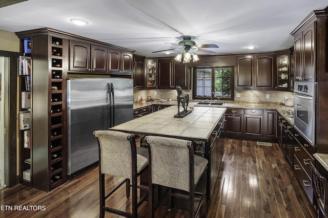 kitchen with a sink, dark wood-style floors, stainless steel appliances, dark brown cabinets, and tile counters