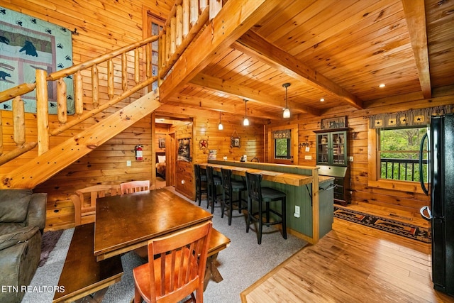 dining area featuring light hardwood / wood-style floors, wood walls, wooden ceiling, bar area, and beam ceiling