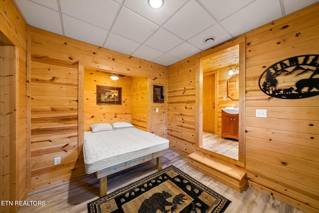 bedroom featuring hardwood / wood-style flooring, a drop ceiling, ensuite bathroom, and wood walls