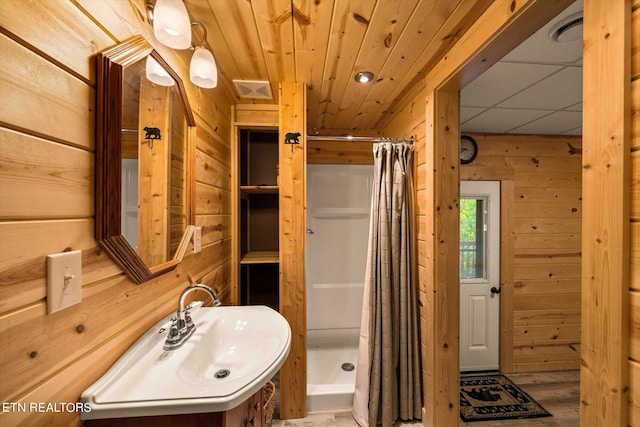 bathroom featuring a shower with shower curtain, wooden walls, and sink