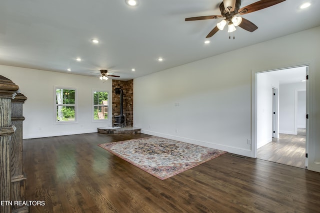 unfurnished living room featuring ceiling fan, dark hardwood / wood-style flooring, and a wood stove