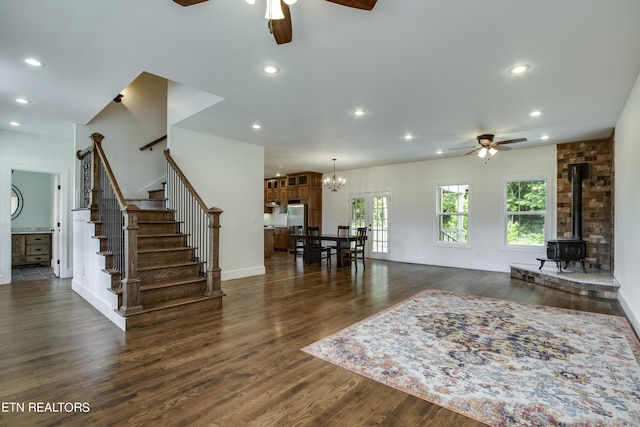 living room with ceiling fan with notable chandelier, a wood stove, and dark wood-type flooring