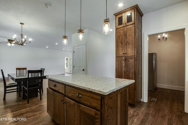 kitchen with dark hardwood / wood-style flooring, hanging light fixtures, light stone countertops, a kitchen island, and ceiling fan with notable chandelier