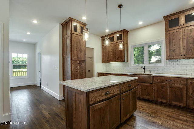 kitchen with dark hardwood / wood-style floors, a kitchen island, decorative backsplash, sink, and light stone counters