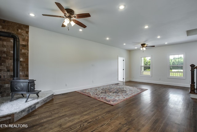 unfurnished living room featuring ceiling fan, a wood stove, and dark hardwood / wood-style floors