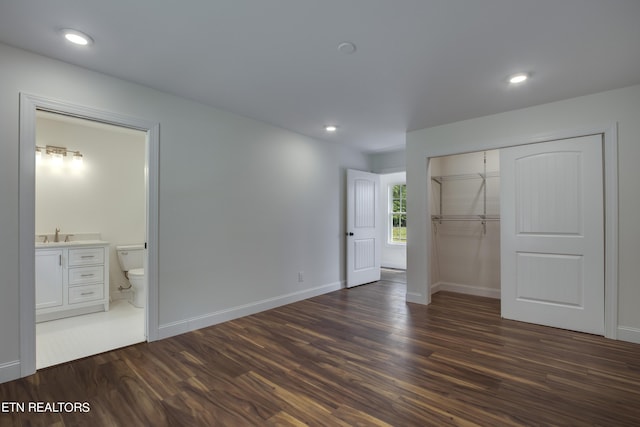 unfurnished bedroom featuring a closet, ensuite bathroom, dark hardwood / wood-style flooring, and sink