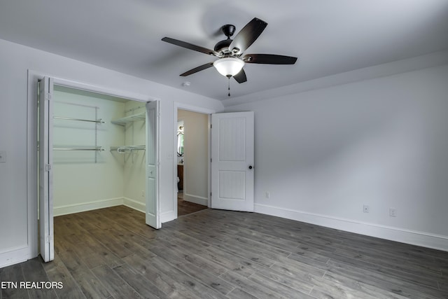 unfurnished bedroom with dark wood-type flooring, ceiling fan, a walk in closet, and a closet