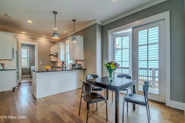 kitchen with light wood-type flooring, kitchen peninsula, stainless steel fridge, white cabinetry, and decorative light fixtures