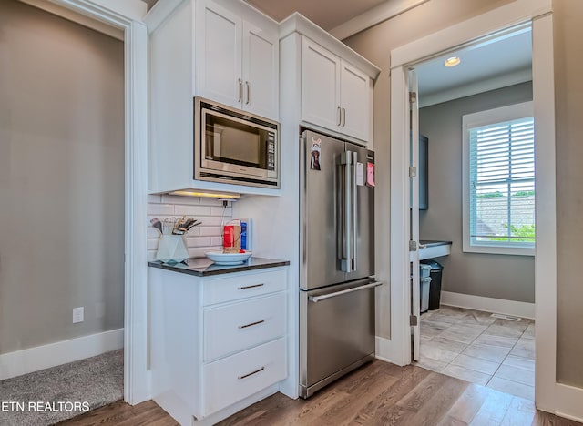 kitchen with light hardwood / wood-style floors, stainless steel appliances, white cabinetry, and decorative backsplash