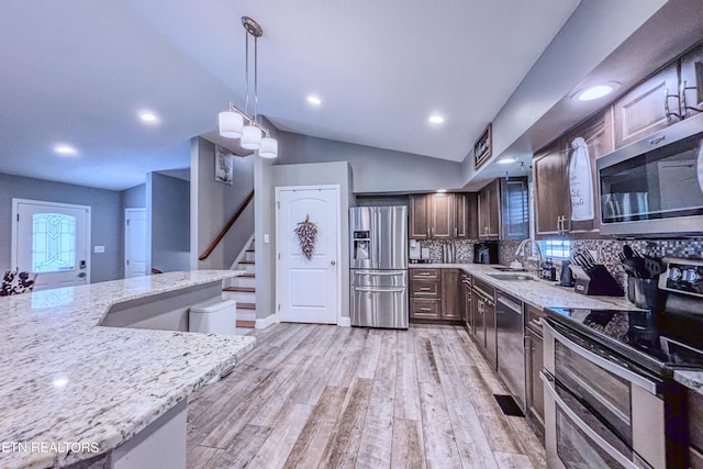 kitchen featuring decorative light fixtures, lofted ceiling, backsplash, appliances with stainless steel finishes, and light stone counters