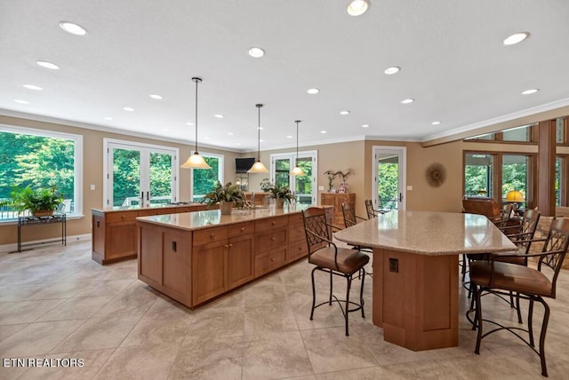 kitchen with pendant lighting, crown molding, light stone countertops, a kitchen breakfast bar, and a large island