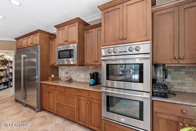 kitchen with light tile patterned floors, tasteful backsplash, light stone countertops, ornamental molding, and built in appliances