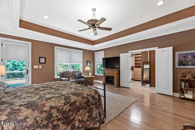 bedroom with ceiling fan, access to outside, a tray ceiling, light hardwood / wood-style flooring, and a spacious closet